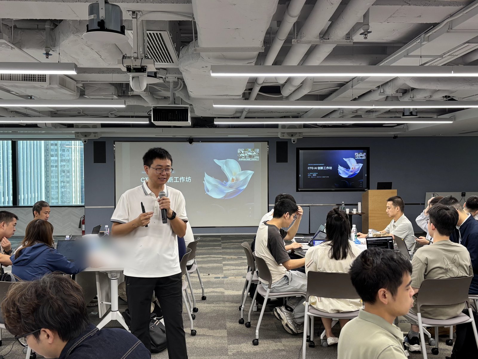 张财华老师主持 AI 创新工作坊，手持麦克风站在投影幕前